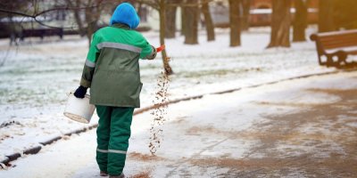 Muž sype chodník pískem z kyblíku