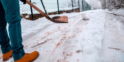 Muž sype lopatou zasněženou cestu