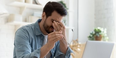 Muž si přidržuje ruce u kořene nosu a v ruce má brýle