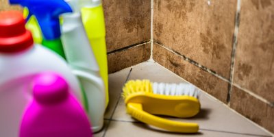 Uklízecí prostředky a kartáč v rohu koupelny s plísní