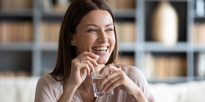 Žena drží v rukou pilulku a sklenici vody