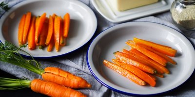 Dvě mrkve i s natěmi a dva talíře s dušenou mrkví nakrájenou podélně na špalíčky