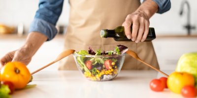 Muž lije do mísy se salátem olivový olej.