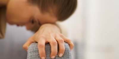 Žena se s vyčerpaným, zoufalým výrazem drží za opěrku křesla