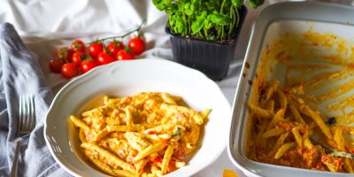 Těstoviny na bílém talíři, okolo je bazalka, rajčata a zapékací mísa