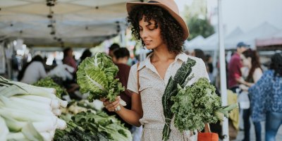 Žena je na trhu a v rukou drží tři různé druhy salátů