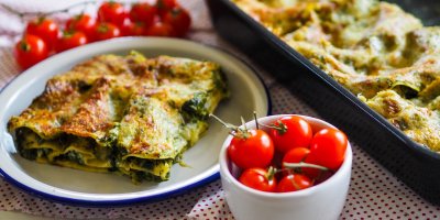 Pekáč s lasagnemi, velká porce na talíři, miska s rajčaty