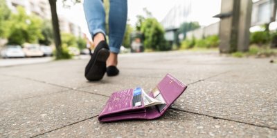 Peněženka ležící na chodníku, v pozadí dámské nohy