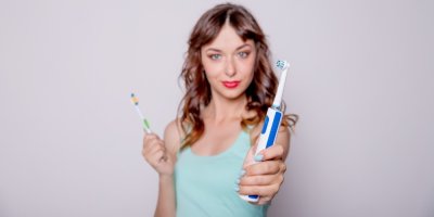 Žena v natažené ruce drží elektrický kartáček, v druhé ruce má manuální kartáček