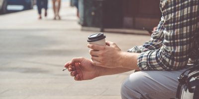 Muž drží kelímek s kávou a cigaretu