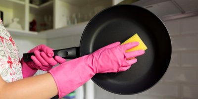 Žena myje v rukavicích pánev houbičkou