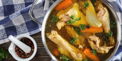 Hrnec kuřecího vývaru na dřevěném stole s ubrouskem