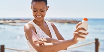 Žena si s úsměvem maže opalovacím mlékem nadloktí.