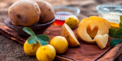 Zářící maska na obličej z bramborové šťávy ve skleněné misce na hnědém povrchu spolu s trochou citronové šťávy, bramborové šťávy a med