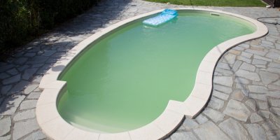 Zapuštěný bazén, ve kterém je zelená voda, nafukovací lehátko