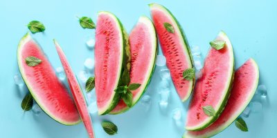 Nakrájené plátky melounu ležící na modrém podkladu, posypané ledem a mátou