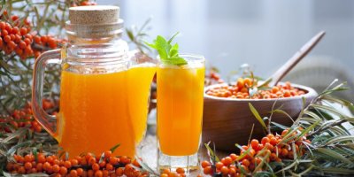 Sklenice a džbán se sirupem z rakytníku a bobule rakytníku kolem nich