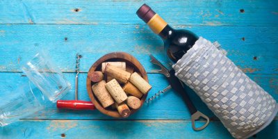 Lahev červeného vína naaranžovaná na stole s vývrtkou a korkovými uzávěry 