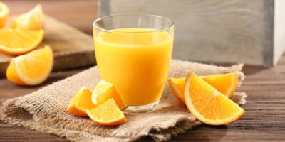 Pomerančový džus ve sklenici, vymačkané pomeranče v pozadí