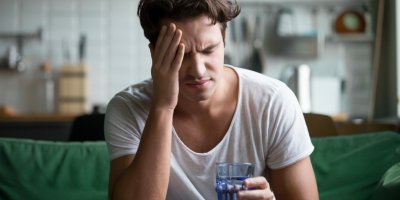 Muže bolí hlava kvůli kocovině a drží sklenici vody
