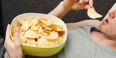 Muž si na gauči dopřává misku chipsů