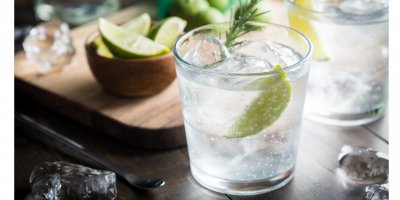 Sklenice gin tonicu s ledem a limetkou, kousky ledu a limetky jsou i kolem ní