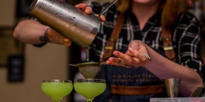 Barmanka připravuje do sklenic míchaný koktejl z shakeru