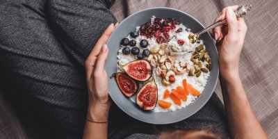 Žena drží na klíně misku s müsli a fíky