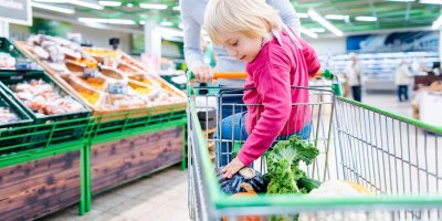 Dítě sedí v nákupním košíku a nakupuje v obchodě s matkou, která ho veze