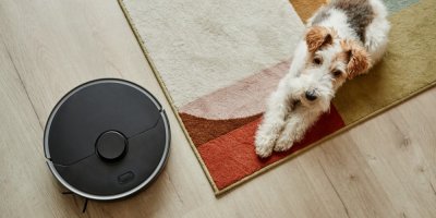 Robotický vysavač vysává podlahu zatímco pes leží na koberci