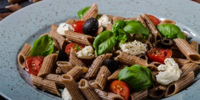 Miska s hnědými těstovinami s olivami, rajčaty, bazalkou a sýrem