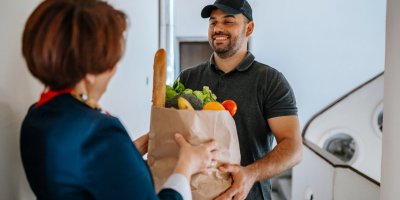 Kurýr předává ženě nákupní tašku s ovocem a zeleninou