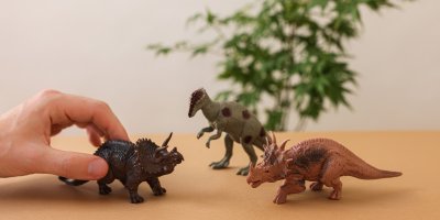 Ruka držící dinosaura, který bojuje proti dalším dinosaurům
