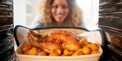 Žena vytahuje z trouby pekáč s kuřetem a brambory