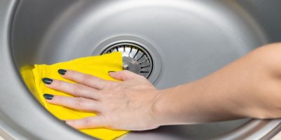 Žena utírá nerezový dřez hadrem