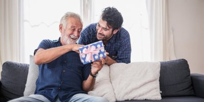 Mladý muž dává dárek staršímu muži, který sedí na gauči