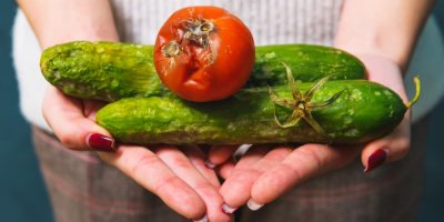 Žena drží v rukou dvě plesnivé okurky a plesnivé rajče.