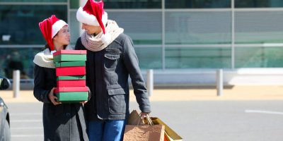 Mladý pár ve vánočních čepicích odchází z nákupního centra s několika taškami a krabicemi