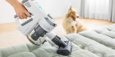 Ruční vysavač drží ruka a čistí gauč