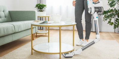 Žena vysává tyčovým vysavačem pod stolem