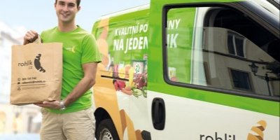 Kurýr společnosti Rohlík nese papírovou tašku s nákupem z dodávky