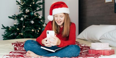 Dívka ve vánoční čepici si prohlíží telefon u stromečku