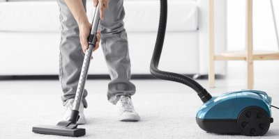 Muž vysává koberec modrým sáčkovým vysavačem