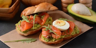 Dva chlebíčky s avokádovou pomazánkou ozdobené vajíčky, uzeným lososem a bylinkami