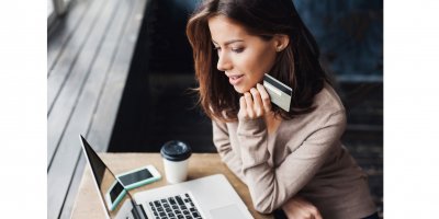 Žena sedí u počítače a drží platební kartu