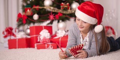 Děvče píše na vánoční kartičku u vánočního stromu