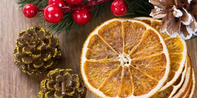 Kolečka sušeného pomeranče naskládaná na sobě, vedle jsou šišky ozdobené třpytkami a umělá větvička jalovce