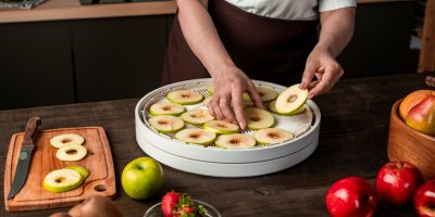 Žena klade nakrájené plátky jablek do sušičky potravin