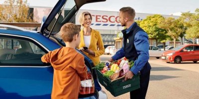 Zaměstnanec Tesco předává ženě na parkovišti nákup 