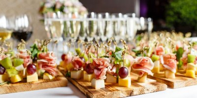 Jednohubky na dřevěném táce a za nimi sklenice se sektem